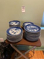 Stack of blue-and-white collector plates on folding table showing front designs and rim year markings