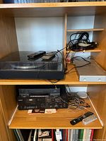 Full shelf view showing turntable on upper shelf, VHS/VCR and cassette deck on lower shelf, DVD player, cables and remotes