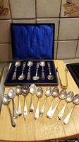 Full view of presentation box with six filigree spoons, assorted spoons and tongs on wooden board