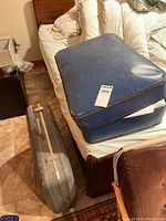 Two vintage suitcases placed next to a bed on the floor, one blue and one gray