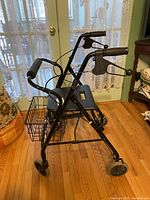 Full view of black Dana Douglas walker showing frame, seat, basket, wheels, and hand brakes.