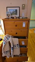 Full view of wooden dresser with three drawers, wool sweater hanging from an open drawer, multiple small items, and framed photos on top of dresser.