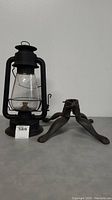 Front view of Liberty Cold Blast lantern beside cast iron Christmas tree stand on a flat surface with lot tag visible.