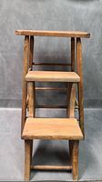 Front view of wooden folding dual-use step stool showing steps and top seat area.