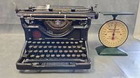 Antique Underwood typewriter and Waymaster letter balance scale side by side on gray surface