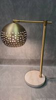 Full view of the desk lamp showing the round marble base and adjustable brushed metal arm with perforated spherical shade.