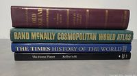 Stack of four large hardcover books showing titles on spine: Old England, Rand McNally Cosmopolitan World Atlas, The Times History of the World, The Home Planet.