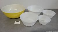 Five bowls arranged in a group showing size and color variation; one large yellow bowl and four white bowls.