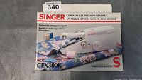 Front of the original packaging for a Singer Cordless Electric Mini Mender Model CEX300K showing product image and branding.