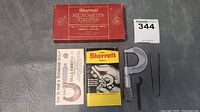 Starrett micrometer caliper with original red box, two instruction manuals, calibration wrench, and gauge tool laid out on a grey surface.