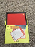 Original box containing the red Logitech Blok protective sleeve for iPad Air 2, placed on carpeted floor.