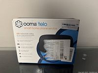 Front side view of the Ooma Telo smart home phone service box showing branding and services offered.