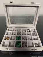 Jewelry case open showing multiple compartments with assorted rings, earrings and one brooch inside