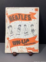 Photo showing original packaging of Beatles Pin Up Screamers from 1964 by Gordon Currie USA, with illustrated caricatures of each band member's face and names in orange and black.