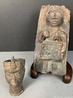 Photo of the cast metal head of Oba and the metal plaque with standing figure on wooden stand.