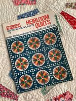Photo of McCalls Needlework & Crafts Heirloom Quilts reference book on colorful hand-stitched quilt background.