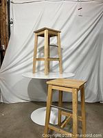 Ikea Bosse wooden bar stools showing natural wood finish, square seats, metal footrests, in front of white backdrop.