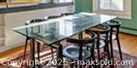 Full side view of the dining table showing the glass top and black stainless steel legs with chairs around it for scale only