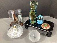 Overview of the lot showing all six items including cat figurine, oil candle, paperweights, and glass window charm on black stand