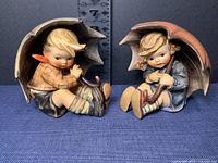 Front view of both the Umbrella Boy and Umbrella Girl M.J. Hummel figurines showing detailed color and condition.