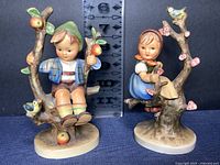 Front view of both Apple Tree Boy and Girl M.J. Hummel figurines with size reference.
