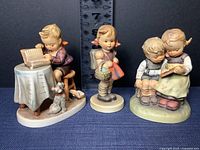 Three M.J. Hummel porcelain figurines displayed together showing school-themed children characters with a dog, basket, and books.