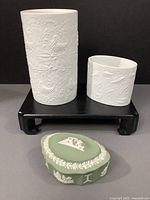 Front-angle photo showing white Rosenthal vases on black stand and green Wedgwood jasperware trinket box in front