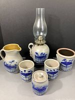 Full set of six Salmon Falls Blueberry Pottery items arranged showing all pieces including oil lamp, pitcher, lidded jar, open jars, and cup with blue hand-painted blueberry basket motif.