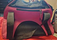 Red soft-sided pet carrier with black mesh panels and shoulder straps shown from the side
