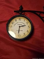 Front view of one clock face showing Grand Central Terminal New York face with black numbers on cream background, mounted on a black metal frame and bracket.