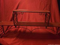 Metal red three-tier storage rack with decorative side scrolls and mesh platform surfaces from front view