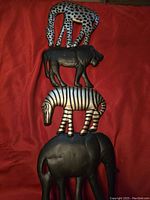 Photo showing stacked wooden safari animal wall decor pieces on red fabric background