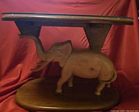 Side view showing the carved elephant base and wooden table top with natural finish.