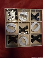 Top-down photo of a wooden tic-tac-toe style board with black X and white O pieces in plastic packaging