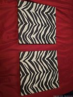 Two square canvas art pieces with black and white zebra stripe patterns placed on red fabric background.