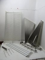 Photo showing all items in the lot including two stainless steel corner shelves, two white plastic-coated shelves, two turkey forks, and two six-hook rails.