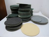 Stacks of circular felt pads in green, grey, black, and beige on white surface.