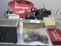 Wide view of sewing machine accessories including Singer buttonholer, motors, pedals, pattern cams, and parts arranged on table.
