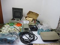 Photo showing a large assortment of sewing machine accessories including motors, buttonholer, controller, foot pedal, pattern cams, and parts arranged on table.