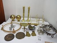 Full view of all mixed brass items spread on a white surface showing decorative brass spheres, columns, miniature table, plaques, bird figurine, carriage, frame, and brass stands.