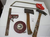 Overall lot view showing handsaw, axe, hammer, measuring tape and carpenter square.