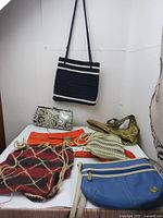 Lot of seven purses on a table including hand knitted, snake skin pattern clutch, and orange envelope clutch.