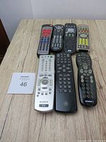 All seven remote controls laid out on a wooden surface, clearly showing brands and button layouts.