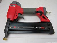 Senco FinishPro 18 gauge finishing nailer showing red and black body with grey grip and attached air hose coupling. Magazine is black and marked FinishPro 18.