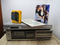 Overview of Sony tape recorder TC-FX33, Panasonic DVD/CD Player S27, yellow Sports Walkman, Titanic VHS tape, and children's cassette tape in original packaging placed on a wooden surface with white background.