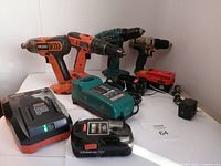Photo showing four cordless drills/drivers, two battery chargers, and three batteries arranged on a white surface.