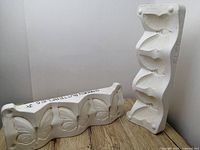 Two white ceramic moulds positioned on a wooden floor, one mould with three butterfly shapes, the other with bird shapes.