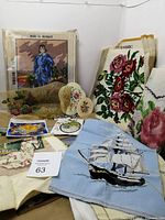 Photo of multiple vintage needlework items including Blue Boy cross stitch kit, floral needlepoints, ship design, and small stitched hearts
