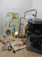 Overall view of vintage lot showing multiple items including metal magazine holder, rotating tie system box, tapestry runner, and various small items on a wooden floor.