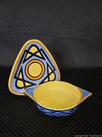Photo of triangular plate and soup bowl displayed separately, showing Art Deco geometric pattern in yellow, blue, black, and orange colors on glossy ceramic.